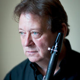 A person with short hair, in a dark shirt, holds a clarinet close to their face and gazes thoughtfully to the side against a softly blurred background. They are appreciating Stravinsky: The Soldiers Tale by the London Symphony Orchestra.